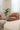 A modern tan leather armchair in a bright, minimalist living room setting with sheer white curtains, a potted green plant, and marble-patterned side tables.